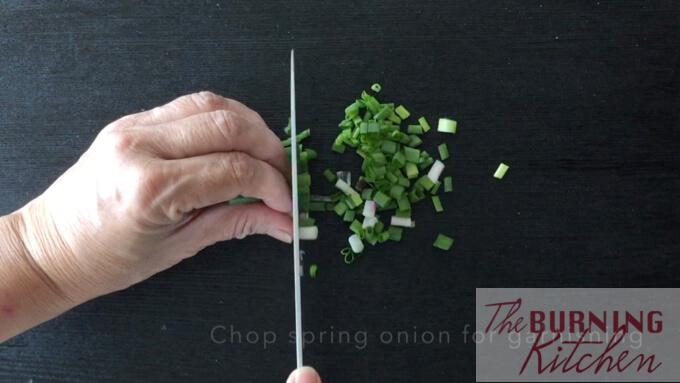 chopping spring onions on black chopping board